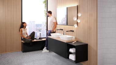 Femme assise sur le rebord d’une fenêtre parlant à un homme dans une salle de bains design, Geberit ONE